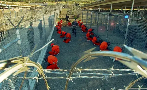 Guantánamo Bay detainees sit in a holding area at Camp X-Ray on January 11, 2002. Image courtesy of the Pentagon by Shane T. McCoy.
