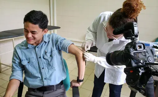 2020 Reporting Fellow Anton L. Delgado&nbsp;grimaces as Raquel Bouth, a Ph.D. student studying microbiology, takes a sample from the olecranal skin on his left elbow. This was the final part of Delgado’s leprosy evaluation that he took after nearly a month of field work in northern Brazil. Image by Moises Silva.&nbsp;Brazil, 2020.
