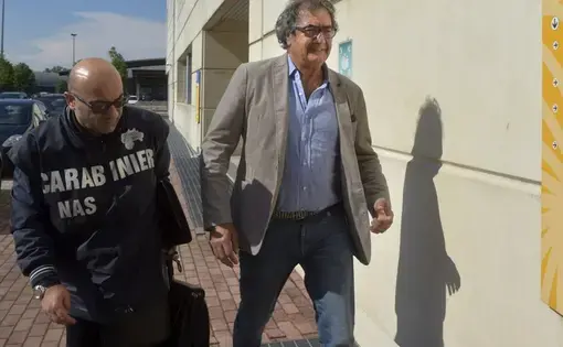 Dr. Guido Fanelli, right, is taken to the Carabinieri headquarters in Parma, Italy, for questioning in an alleged pharmaceutical kickback scheme on Monday, May 8, 2017. That morning, police jolted Fanelli out of bed. It was a spectacular fall from grace for a man who appeared days before on a popular television show to promote painkillers. Image by AP Photo/Marco Vasini. Italy, 2017.