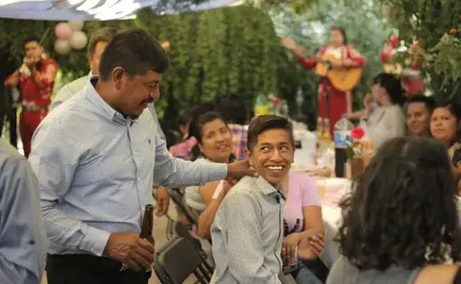 Winny Contreras laughs with his son Ricardo as a mariachi band plays at his eldest daughter's graduation party in their home in Mexico. Image by Ingrid Holmquist. Mexico, 2018.