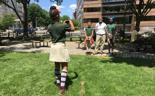 A Stanton Elementary School student takes a photo of two other students and a person they interviewed in Dupont Circle on June 1, 2017. Image by Allison Shelley. United States, 2017.