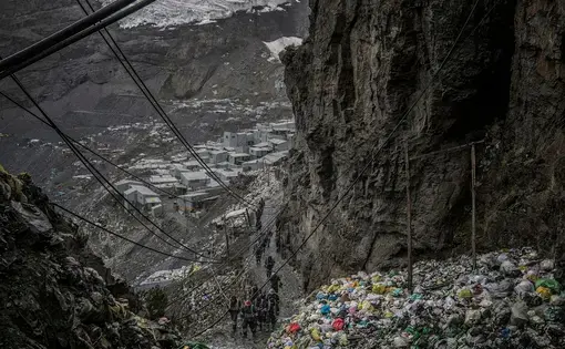 Workers return from the mines for lunch along a pathway etched into a cliff, past a mountain of garbage, at the La Rinconada gold mine complex in Peru. Peru,2019. Image by James Whitlow Delano.