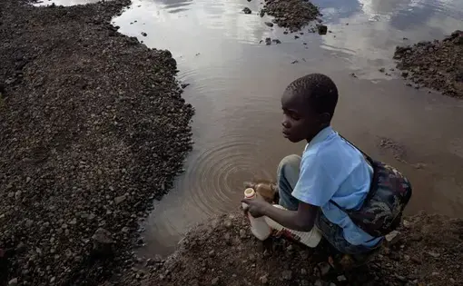 Brian Jovo, 14, collects contaminated water from a pool at Kabwe's Black Mountain. Image by Larry Price. Zambia, 2017. Brian Jovo, 14, collects contaminated water from a pool at Kabwe's Black Mountain. Image by Larry Price. Zambia, 2017.