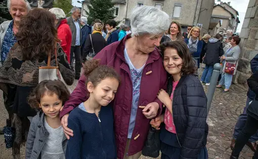 Michelle Baillot brings Touana (5), Schkourtessa (7) and Erlina Sélimi (10) to France’s World War II Victory Day at Le Chambon-sur-Lignon’s town’s square.  The girls are from a Kosovar refugee family that Baillot has been close to now for ten years. “I tell them that you are not from here, so you are going to have to be better than everyone else.” Image by Lucian Perkins. France, 2018.