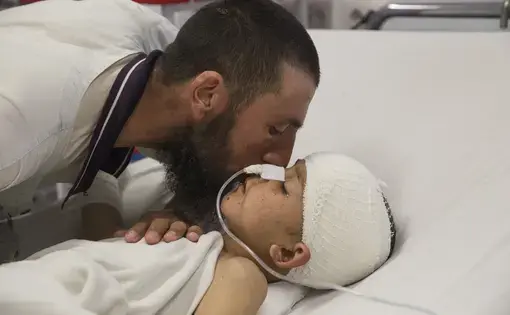 Abdul Kabir kisses his son, Noor Ahmad, 8, who is unconscious with a severe brain injury from an improvised explosive device (shell injury) from Mazar-E-Sharif Kabul on March 12, 2016. His father was also injured but recovered. Image by Paula Bronstein. Afghanistan, 2016.