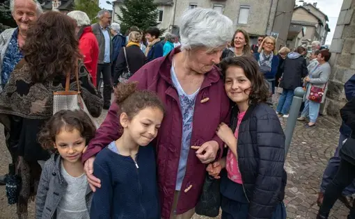 Michelle Baillot brings Touana (5), Schkourtessa (7) and Erlina Sélimi (10) to France’s World War II Victory Day at Le Chambon-sur-Lignon’s town’s square.  The girls are from a Kosovar refugee family that Baillot has been close to now for ten years. “I tell them that you are not from here, so you are going to have to be better than everyone else.” Image by Lucian Perkins. France, 2018.