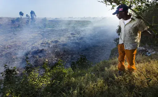 A man stands on the edge of a precipice overlooking Dandora, Korogocho’s 30-acre massive dump of smoldering garbage. People scavenge through the dump looking for anything of value. Image by Mark Hoffman. Kenya, 2017.