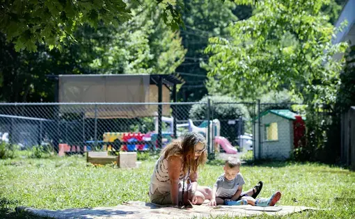 Bell’s School teacher Angela Mehaffey reads a book with Elliot Fink, 2, on a blanket outside the Fletcher preschool June 22. Image by Angeli Wright/Asheville Citizen Times/North Carolina News Collaborative. United States, 2020.