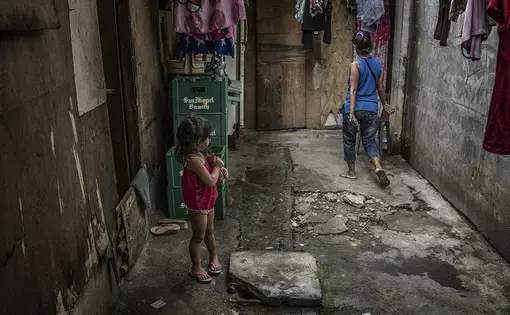 Josie, a 43-year-old former "shabu" (methamphetamine) user and pusher, navigates the living area of the bar in a rural area of the Philippines, where she works as a housekeeper. She is being watched by one of the bar worker's daughters. Recently Josie fled the Market 3 slum in Navotas because she feared assassins might come to execute her. Her drug-related activities were well known in Market 3 and many others have been executed for similar activities. Image by James Whitlow Delano. Philippines, 2017.