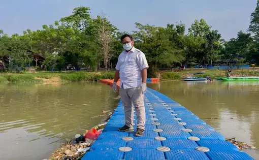 Ade Yunus, founder of environmental organisation Bank Sampah Sungai Cisadane (Cisadane River Waste Bank) or Banksasuci, stands on a floating boom used to collect waste from the Cisadane River in Tangerang, Indonesia. Image by Adi Renaldi. Indonesia, undated.