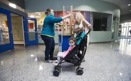 Guest Services Manager Hillary Parks, left, conducts a wellness check-in with Susan Sunday of Rockford, right, and Serafina Davila, in the stroller, before they enter the Discovery Center on Thursday in Rockford. Staff and visitors are taking health safety precautions while the museums limits public access. Image by Scott P. Yates/Rockford Register Star. United States, 2020.