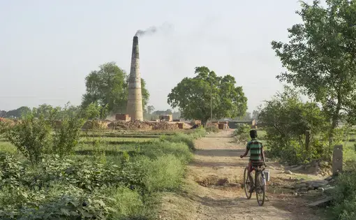 A boy rides a bike towards a brick kiln outside of Varanasi, India. Many kilns in the country rely on bonded labor. Image by Ann Hermes. India, 2016.