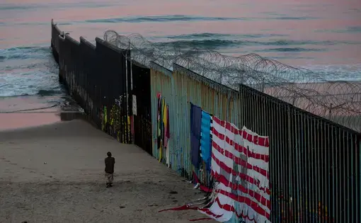 In Tijuana, a man walks at sunrise along the border fence where it meets the Pacific Ocean. Image by Erika Schultz. Mexico, 2019.