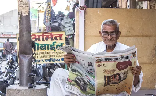 A Rajasthani man reads a local newspaper in the streets outside the Jaisalmer fort. Image by Ihsan Iqbal / Shutterstock.com. India, 2016.