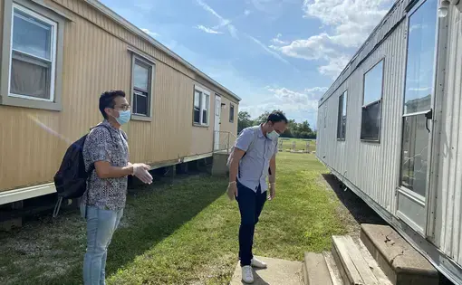 FLOC members Lorenzo Zamora (left) and Braulio Franco (right) wait outside for a farmworker to answer the door during their visit to Liskai Farms migrant camp. Image by Areeba Shah. United States, 2020.