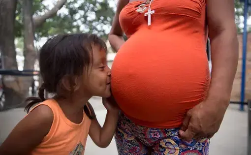 Venezuelan migrant Fabiana Correa Martinez, 4, kisses the belly of her pregnant mother Nairobi Correa Martinez in a migrant soup kitchen in Cucuta, Colombia on Feb. 9, 2019. Image by Megan Janetsky. Colombia, 2019.