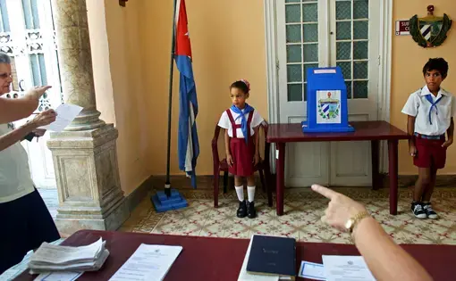 Children wearing the uniform of Communist youth are prepared to salute “Votó!” (“He voted!”), as a woman places her ballot in Cuba’s Elecciones Parciales (Partial Elections). The vote was to elect delegates to the Municipal Assemblies of People’s Power, the country’s unicameral parliament, on April 19, in Havana. The delegates function as district representatives for a two-and-a-half-year term. Image by Yana Paskova. Cuba, 2015. Children wearing the uniform of Communist youth are prepared to salute “Votó!” (“He voted!”), as a woman places her ballot in Cuba’s Elecciones Parciales (Partial Elections). The vote was to elect delegates to the Municipal Assemblies of People’s Power, the country’s unicameral parliament, on April 19, in Havana. The delegates function as district representatives for a two-and-a-half-year term. Image by Yana Paskova. Cuba, 2015.