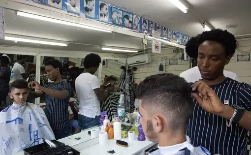 In this Wednesday, Aug. 8, 2018 photo, Eritrean migrant Gharmay Negassi works at a barbershop in Tel Aviv, Israel. African migrants coming into Israel have been detained, threatened with deportation, and faced hostility from lawmakers and residents. Now, they face another burden: a de facto 20 percent salary cut that has squeezed them financially and driven them further into poverty. Image by Caron Creighton. Israel, 2017. In this Wednesday, Aug. 8, 2018 photo, Eritrean migrant Gharmay Negassi works at a barbershop in Tel Aviv, Israel. African migrants coming into Israel have been detained, threatened with deportation, and faced hostility from lawmakers and residents. Now, they face another burden: a de facto 20 percent salary cut that has squeezed them financially and driven them further into poverty. Image by Caron Creighton. Israel, 2017.