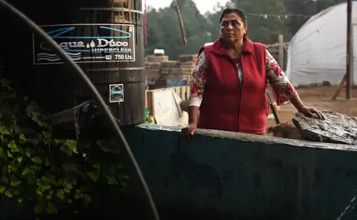 Margarita Reyes takes a break after finishing her typical water gathering routine, which requires her to haul a large pump down to a nearby river. Reyes has lived on the same property her entire life and has watched the Cutzamala System invade her community. She has never had running water in her home despite the proximity of the system. Image by Meg Vatterott. Mexico, 2018. Margarita Reyes takes a break after finishing her typical water gathering routine, which requires her to haul a large pump down to a nearby river. Reyes has lived on the same property her entire life and has watched the Cutzamala System invade her community. She has never had running water in her home despite the proximity of the system. Image by Meg Vatterott. Mexico, 2018.