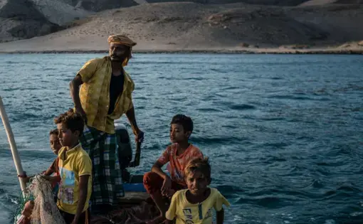 Shafai Saleh Hadi drives a friend's boat along the coast of Bir Fuqum, searching for fish with his sons. Image by Alex Potter. Yemen, 2018.