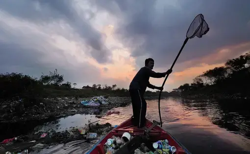 Deni Riswandani pushes his canoe filled with scavenged trash toward his village on the banks of the Citarum River. Demi travels up to eight miles a day on the polluted river to collect plastic and other recyclables. Image by Larry C. Price. Indonesia, 2016.