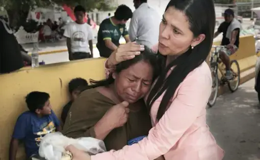 Gladys Edil Caas, a local Mexican volunteer who delivers water, blankets and other needs to migrants camped out by the bridge, consoles a Guatemalan woman during a visit to the camp. Image by Jose A Iglesias. Mexico, 2019.