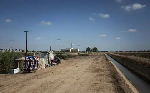 This July 24, 2020, photo shows a homeless encampment near a canal in El Centro, Calif. As support services have dwindled amid the COVID-19 pandemic, some homeless people in Imperial County have resorted to bathing in irrigation canals. Homelessness looks different in different parts of the U.S., especially in rural agricultural regions such as Imperial County. Image by Anna Maria Barry-Jester/KHN and the Howard Center For Investigative Journalism via AP. United States, 2020.