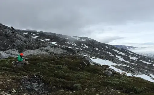 Science reporter Ari Daniel on assignment in Greenland. Helheim glacier, one of Greenland's largest glaciers, is off to the right. Image by Kate Raisz. Greenland, 2015. Media file: ariorange.jpg