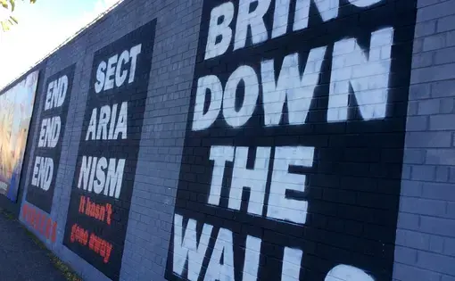 A mural reading 'End Sectarianism: Bring Down The Walls' on the Falls Road mural wall in Belfast. Image by Julia Canney. Northern Ireland, 2018. A mural reading 'End Sectarianism: Bring Down The Walls' on the Falls Road mural wall in Belfast. Image by Julia Canney. Northern Ireland, 2018.