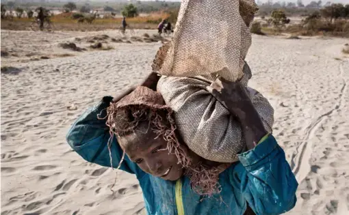 Daniel (11) carries a bag of cobalt on his back. He works in a mine ferrying sacks of cobalt to a depot. Image by Sebastian Meyer. Democratic Republic of Congo, 2018.