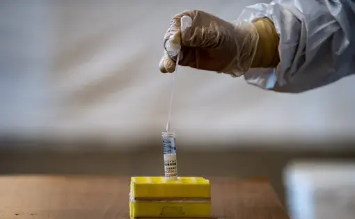 A medical staff member wearing protective clothing puts a swab into a container during demonstration of the Polymerase Chain Reaction (PCR) swab test for COVID-19 in Tokyo on May 8, 2020. Image by Philip Fong/AFP. Japan, 2020.