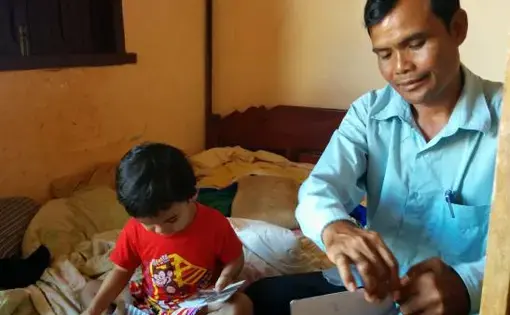 Journalist Sa Piseth at home with his son, going through photos of illegal logs. Image by Saul Elbein. Cambodia, 2014.