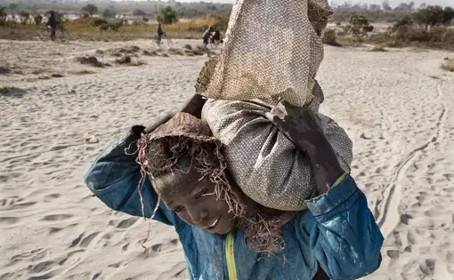 Daniel (11) carries a bag of cobalt on his back. He works in a mine ferrying sacks of cobalt to a depot. Image by Sebastian Meyer. Democratic Republic of the Congo, 2018.