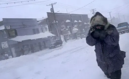 In this Feb. 23, 2019, photo, a woman shields her face from the wind during a snow storm as she walks on Front Street in Nome, Alaska. Image by Wong Maye-E. United States, 2019.