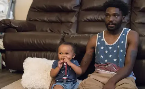 Theron Carson sits on the floor with his daughter watching cartoons. Carson was charged with trafficking marijuana and had $1,200 seized from his home after the police smelled weed coming from his Newburg apartment and conducted a search. Image by J. Tyler Franklin. United States, 2019.