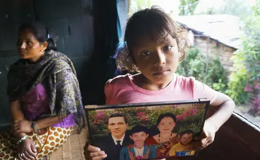 Lozan B.K., 9, holds a digitally-altered photo of her family. Her father, Giri Prasad B.K., who was added to the photo, went to Qatar as a migrant worker before Lozan was born. He was injured there in a road accident and has been in a vegetative state since 2011. Image by Yam  Kumari Kandel. 2016.