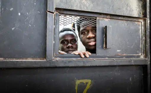 Detainees from West Africa peer out of their overcrowded cell in the al-Nasr detention center in Zawiya, Libya, where migrants intercepted by the Coast Guard in Zawiya are warehoused indefinitely. Image by Peter Tinti. Libya, 2017.