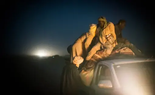 Migrants pile onto the back of a pickup truck bound for Libya on the outskirts of Agadez, Niger. The trip across the Sahara, where temperatures can soar above 120 degrees Fahrenheit, typically takes around three days. Image by Nichole Sobecki. Niger, 2017.
