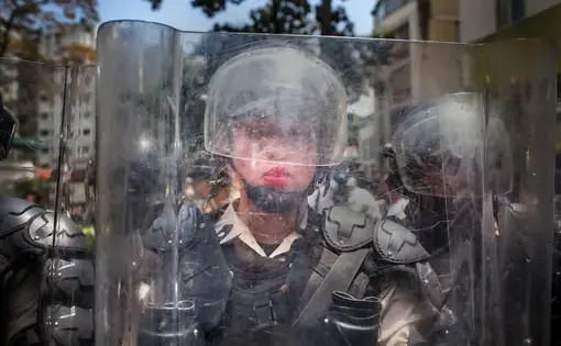 A National Police officer behind a riot shield is pushed backward by a crush of demonstrators during the March of the Empty Pots in Caracas in 2014, which coincided with International Women’s Day. Image by Natalie Keyssar. Venezuela, 2014.