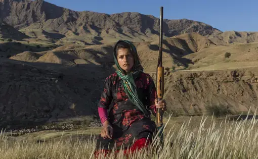 Masoumeh Ahmadi, 14 years old, wants to be called by the name Golbahar since Masoumeh is an old-fashioned name, not popular among the young generation. She stands in Chamsoor lands in Khuzestan Province holding a gun. It is common among Bakhtiaris for each person to own a gun. Each family might have three or 4fourguns that are mostly for men. Women—with the approval of their husband and father—can have their own guns after they marry . Many of them receive their gun as a gift from their husbands after they give birth to their first son. Masoumeh borrowed her mother’s gun occasionally. Image by Newsha Tavakolian. Iran, 2018. Masoumeh Ahmadi, 14 years old, wants to be called by the name Golbahar since Masoumeh is an old-fashioned name, not popular among the young generation. She stands in Chamsoor lands in Khuzestan Province holding a gun. It is common among Bakhtiaris for each person to own a gun. Each family might have three or 4fourguns that are mostly for men. Women—with the approval of their husband and father—can have their own guns after they marry . Many of them receive their gun as a gift from their husbands after they…