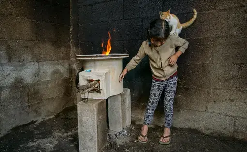 Tania López, 7, plays with her cat in a room whose walls were blackened by an old open fire; the new stove, provided by StoveTeam International, is efficient and safe to touch. Image by Lynn Johnson. Guatemala, 2017.