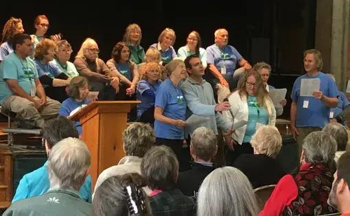 Hands Across the Hills participants sing at public forum in Leverett Elementary School’s auditorium as other group members from Kentucky and Leverett look on. Image by Richie Davis. United States, 2019.