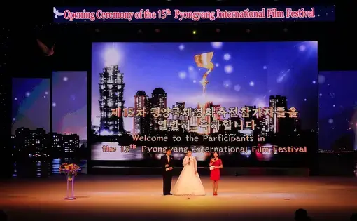 The three hosts on stage during the opening ceremony of the 15th Pyongyang International Film Festival. A sculpted dove in the top left signifies the festival's mission of peace. Image by Laya Maheshwari. North Korea, 2016.