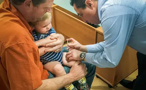 Erik Vance holds his son while a pediatrician administers vaccinations. Image courtesy Erik Vance. Mexico, 2017.