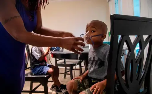 Vantisha Williams, left, adjust a nebulizer mask on the face of her 4-year-old son Jonathan, right, as he and his twin brother Jeremiah receive nebulizer treatments for asthma at their home in Bayboro Thursday, Aug. 20, 2020. Eastern North Carolina has more people making trips to hospital emergency departments for asthma treatments than in any other part of the state, researchers at East Carolina University reported. Image by Travis Long / The News &amp; Observer. United States, 2020.