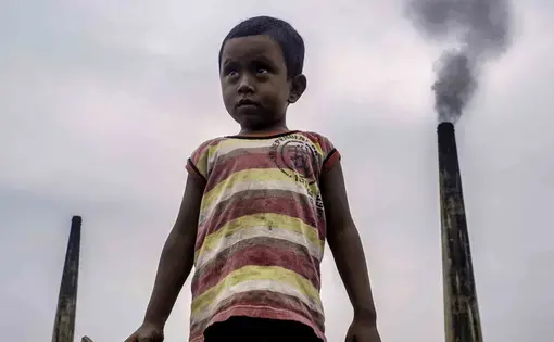 Four-year-old Nayem often plays atop large piles of coal used to fire kilns at a brick factory at the edge of Dhaka, Bangladesh. The chimneys from such factories contribute to some of the worst air pollution in the world. Image by Larry C. Price. Bangladesh, 2018.