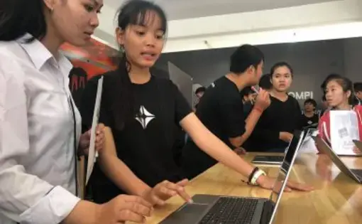 Young women attending the BarCamp ASEAN 2018 expo in Phnom Penh test the KOOMPI laptop. Image from Facebook/KOOMPI. Cambodia, 2018.