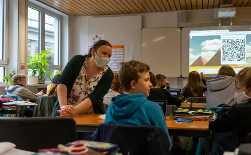 Teacher Inga Deppa works with students in an English class at Jacobishule in Kalletal, Germany. Masks were optional for students when they were seated at their desks, but the regional health authority has since tightened mask rules for older students. Image by Ryan Delaney. Germany, 2020.