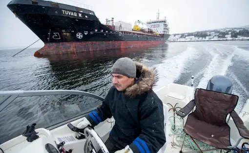 Karl Michelin speeds past a fuel tanker docked at the Rigolet dock for one of two yearly fuel drops on November 10, 2019. Image by Michael G. Seamans. Canada, 2019.