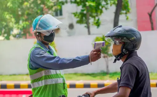 A medical worker in Jamshedpur checks the body temperature of a biker with an infrared thermometer gun for COVID-19 symptoms. Image by ArnavIG / Shutterstock. India, 2020.
